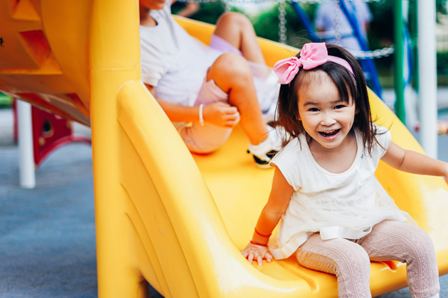 young girl of asian descent takes a brain break by sliding down slide on playground smiling